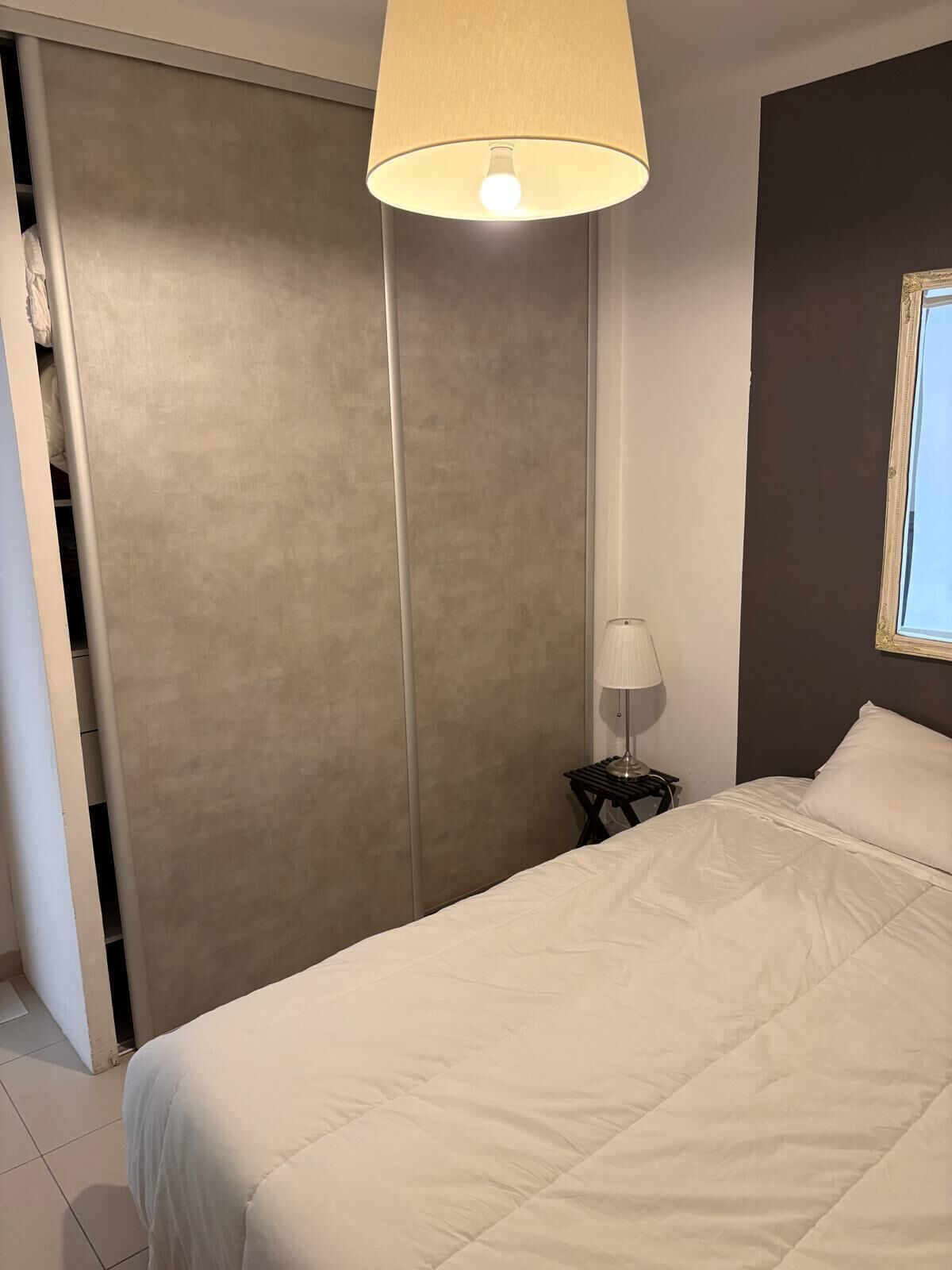Een slaapkamer met een bed, een bedlampje, een kledingkast en een raam.