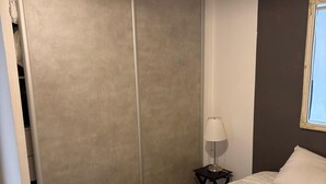 Un dormitorio con cama, lámpara de noche, armario y ventana.