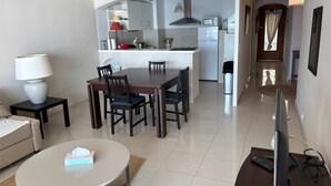 Una sala moderna con una mesa de comedor, sillas, sofá, televisor y una cocina con armarios y electrodomésticos.