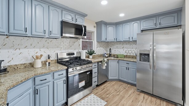 A kitchen with light blue cabinets, stainless steel appliances, a granite countertop, and a white backsplash. - Duplx 6BD-3BH- 3 Parking (West New York)