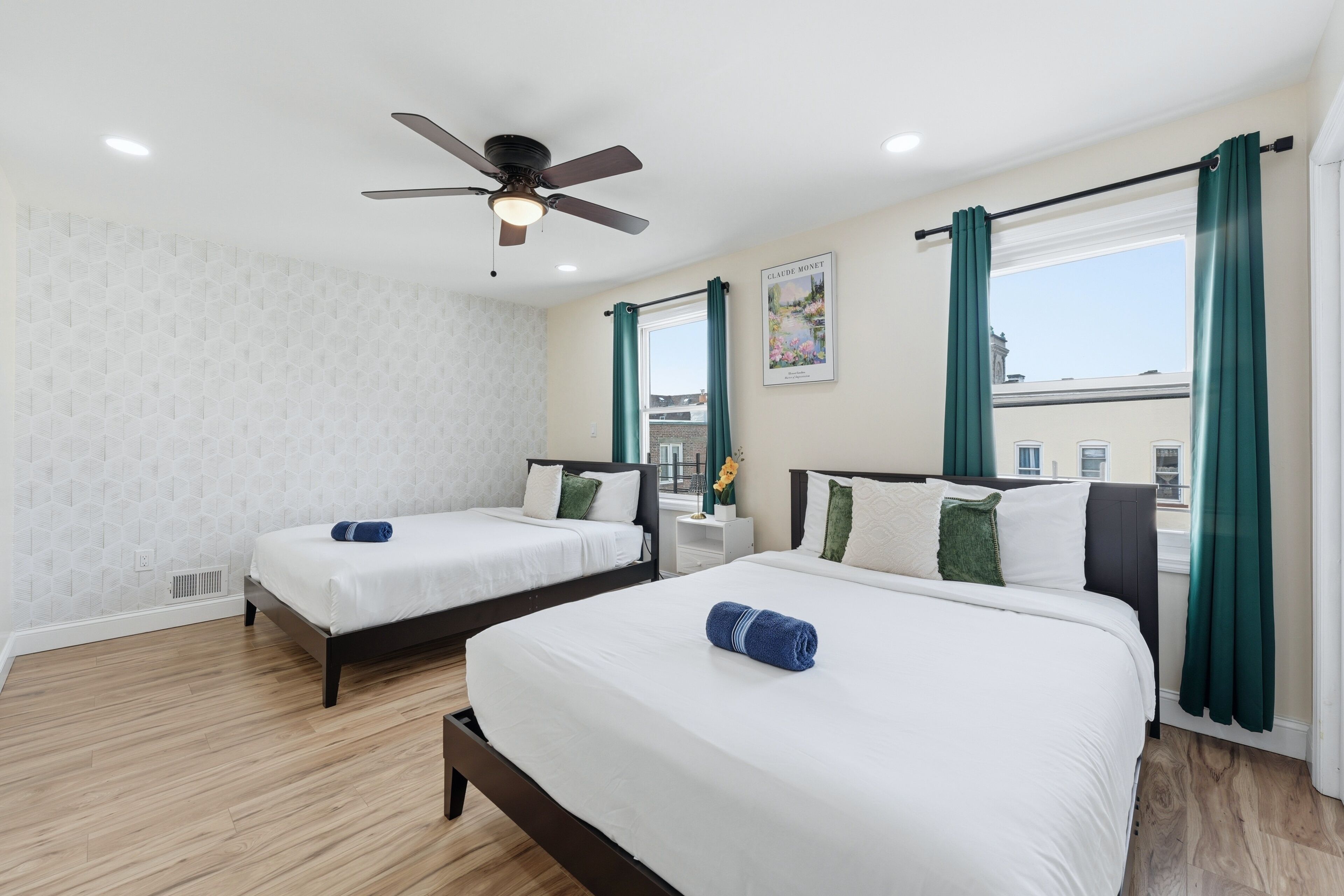 Une chambre d’hôtel avec deux lits, un ventilateur de plafond, une fenêtre avec des rideaux et une œuvre d’art accrochée au mur.