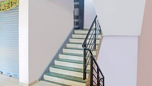 A staircase with glass steps and black railings, leading to a landing with a closed shutter door. - Deluxe Bhagalpur Railway Junction (Bhāgalpur)