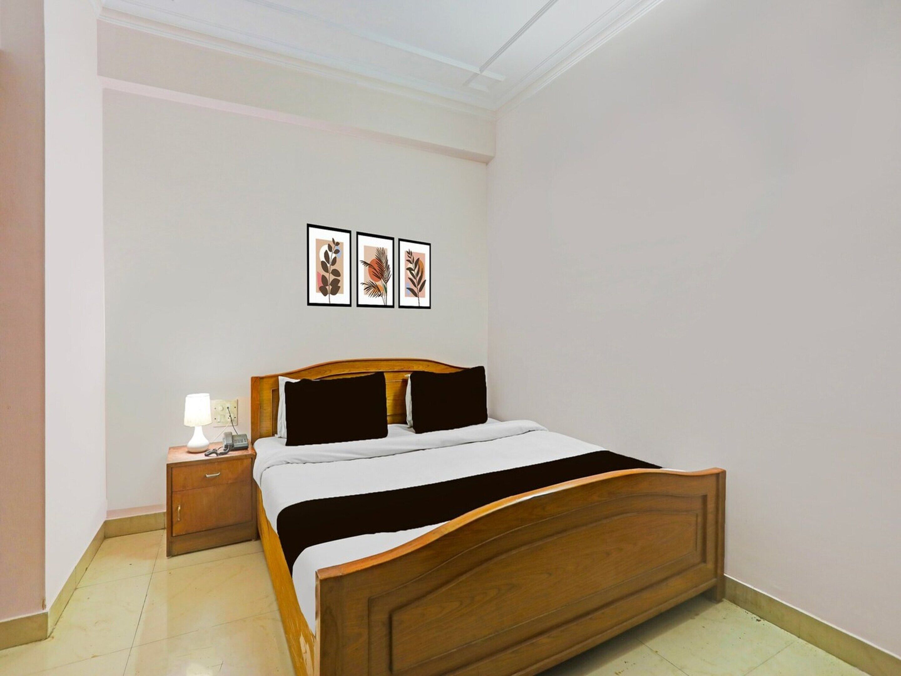 Un dormitorio con una cama de madera, una mesita de noche con una lámpara, y tres cuadros en la pared.