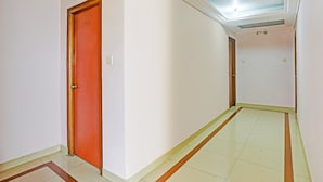 A hallway with a red door, white walls, and a tiled floor. - Deluxe Bhagalpur Railway Junction (Bhāgalpur)