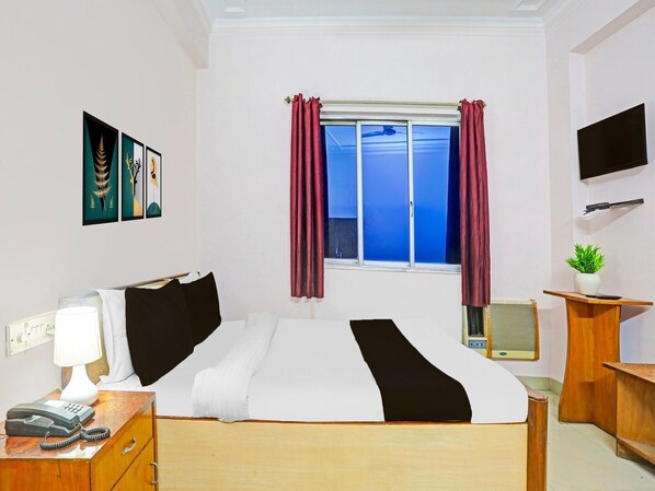 A hotel room with a bed, a desk with a telephone, a TV mounted on the wall, and a window with curtains. - Deluxe Bhagalpur Railway Junction (Bhāgalpur)