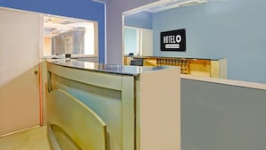 A hotel reception area with a counter, a sign reading 'HOTELO Company Serviced,' and a window providing natural light. - Deluxe Bhagalpur Railway Junction (Bhāgalpur)