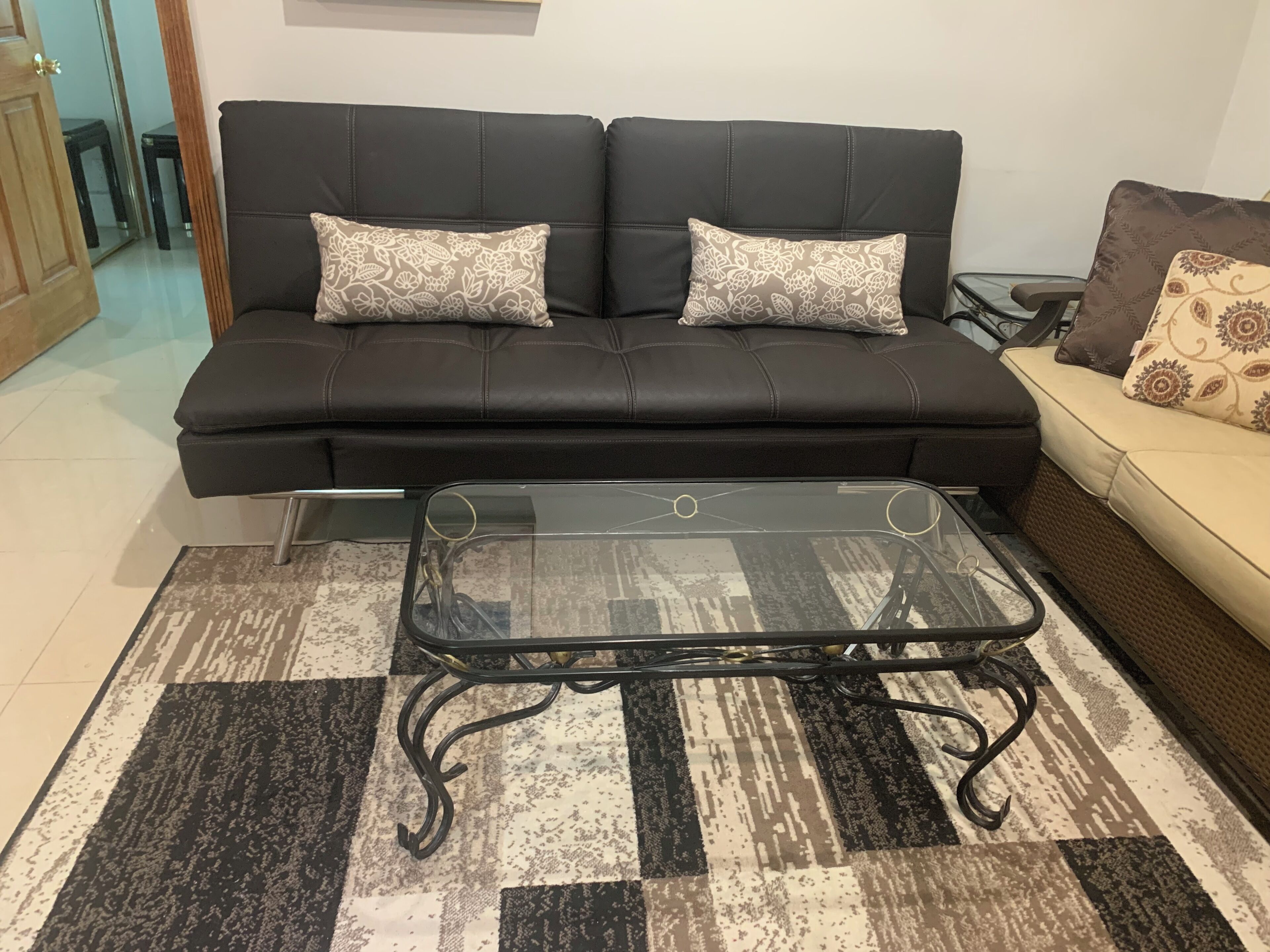 Un canapé en cuir noir agrémenté de coussins à motifs, une table basse en verre et un tapis à carreaux.