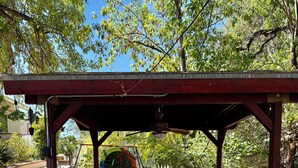Un espacio al aire libre techado con un conjunto de columpios, un banco y un pequeño jardín.