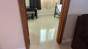 Una habitación con piso de baldosas, una cama con estructura metálica, una mesa de madera y una silla.