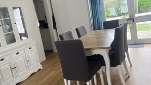 A dining area with a wooden table and chairs, a white cabinet, and a large window with curtains. - Quiet house near the ocean (Saint-Hilaire-de-Riez)