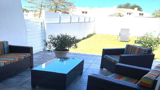An outdoor patio area with wicker furniture, a glass-top table, and a potted plant. - Quiet house near the ocean (Saint-Hilaire-de-Riez)