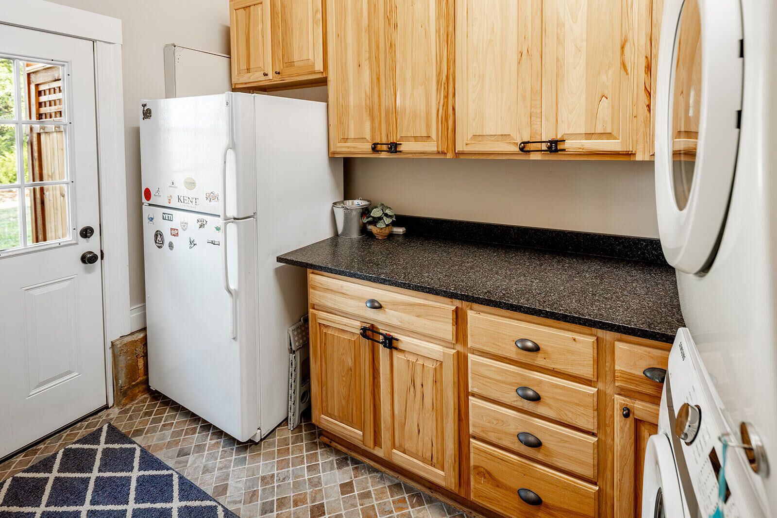 A compact kitchen with a white refrigerator, wooden cabinets, a granite countertop, and a tiled floor.