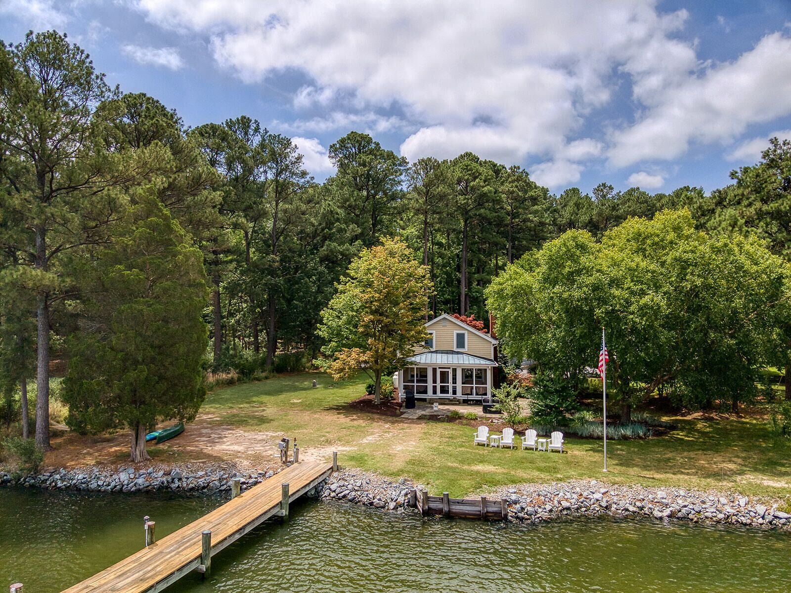 A lakeside cabin with a dock, surrounded by trees and a flag.