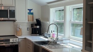 A modern kitchen with white cabinetry, a stainless steel oven, a microwave, and a coffee maker. - Coastal cottage by the sea in Plymouth, MA with private beach access (Plymouth)