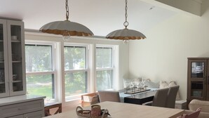 A kitchen with a central island, pendant lights, a dining area with chairs, and a view through large windows. - Coastal cottage by the sea in Plymouth, MA with private beach access (Plymouth)