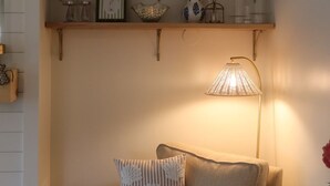 A cozy living room with a sofa, a lamp, and shelves with various decorative items. - Coastal cottage by the sea in Plymouth, MA with private beach access (Plymouth)