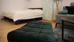 Ett rum med en säng, en grön pall, en grå soffa, ett trägolv och en lampa.