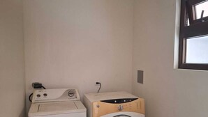Een wasserij met twee wasmachines, een raam en een lichtschakelaar op de muur.