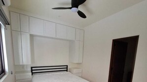 Een slaapkamer met een bed, witte kasten, een plafondventilator en een houten vloer.