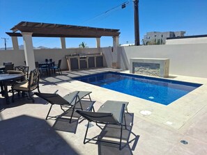 Ein Schwimmbecken mit Liegestühlen, einem Grillbereich und einer Pergola.
