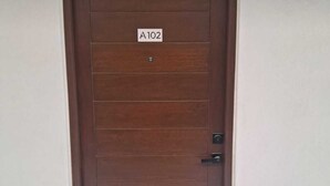 Een bruine deur met een bordje met de tekst 'A102' en een welkomstmat bij de ingang.