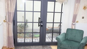 A room with a green armchair, a grey rug, and a sliding glass door leading to an outdoor area with a bench and plants.