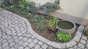 A garden bed with plants and flowers, a stone pathway, and a small water feature.