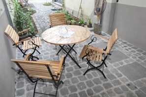 Une table ronde recouverte d’une nappe en dentelle, entourée de chaises en bois dont les pieds sont en métal.