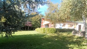 Una propiedad residencial con un césped bien cuidado, un árbol grande y una casa con la puerta principal y ventanas visibles.