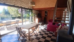 Una habitación con piso a cuadros, muebles de madera, una mesa, sillas, un sofá, una chimenea y vistas amplias a través de grandes ventanales.