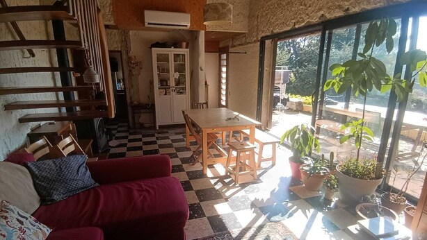 Una habitación con piso a cuadros, un sofá rojo, una mesa de comedor de madera y un ventanal con plantas afuera.