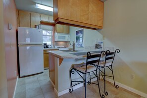 A compact kitchen with a refrigerator, microwave, and stove. There is a small dining area with a chair and a table. - Downtown Condo. 2 sept living areas. Free parking (Hood River)