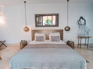 Un dormitorio con una cama, dos mesitas de noche, una lámpara colgante, un espejo y una obra de arte en la pared.
