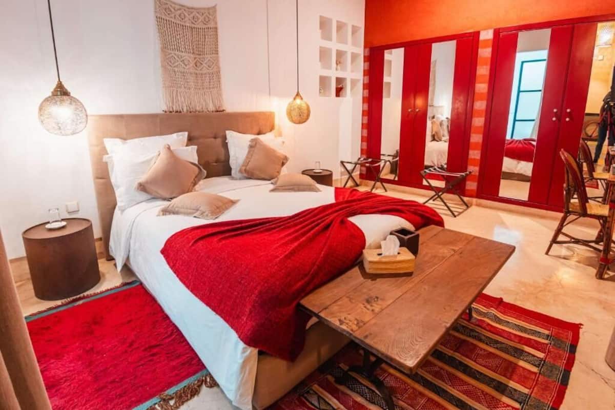 Een slaapkamer met een bed, nachtkastje, lamp en een rode accentmuur.