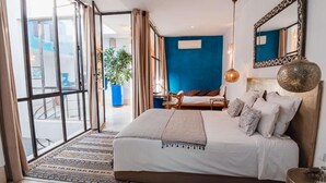 A bedroom with a large bed, a blue accent wall, a hanging light fixture, and a view through a glass door. - Riad La source du Désert (Marrakech)