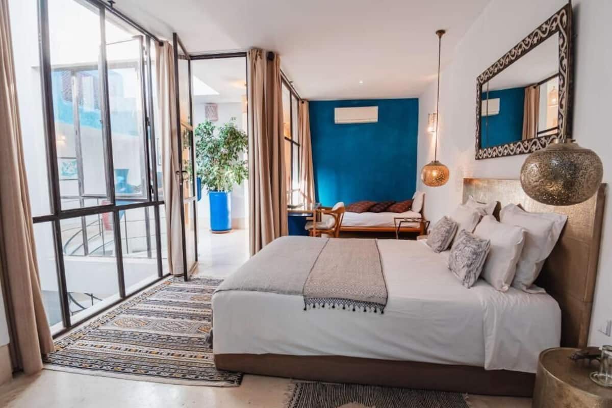 Slaapkamer met een groot bed, een blauwe accentmuur, een hanglamp en uitzicht door een glazen deur.