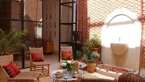 A cozy interior with a seating area, a small table with a vase, and a brick wall with a circular window. - Riad La source du Désert (Marrakech)