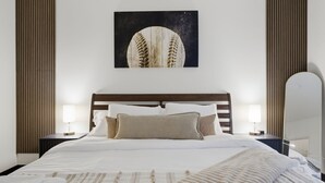 Un letto rifatto con cura, una testiera, due comodini con lampade e un'opera d'arte appesa al muro.