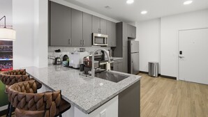 Una cucina moderna con mobili grigi, un forno a microonde in acciaio inossidabile e un lavello. Sono presenti due sgabelli da bar dal design particolare.