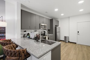 Une cuisine moderne avec des meubles gris, un four à micro-ondes en acier inoxydable et un évier. On y trouve deux tabourets de bar au design original.