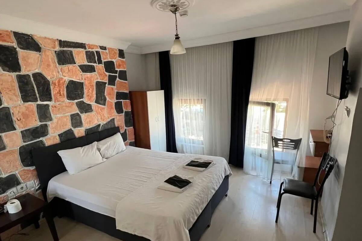 A bedroom with a stone wall, a bed, a desk, and a chair.