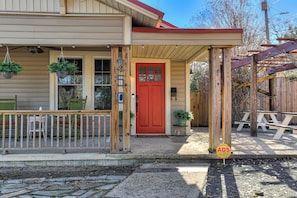 A wooden house with a red door, a porch with chairs, and a sign indicating 'ADS.'