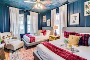 A bedroom with two beds, a ceiling fan, and artwork on the walls.
