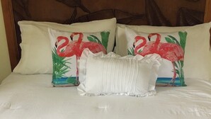 A bed with white bedding, two pillows with a flamingo design, and a headboard with a leaf pattern. - Cozy 1-bedroom bungalow in charming Pleasant Harbour, Morgan’s Bluff with AC (Morgan’s Bluff)