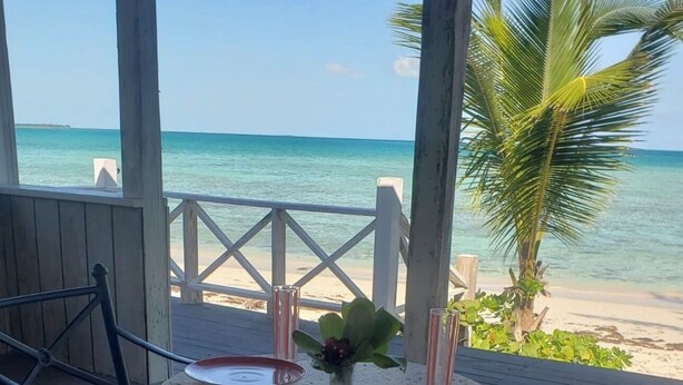 A wooden deck with a round table and chairs, overlooking a beach and ocean. - Cozy 1-bedroom bungalow in charming Pleasant Harbour, Morgan’s Bluff with AC (Morgan’s Bluff)