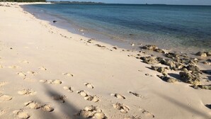 A sandy beach with footprints and rocks, clear blue water, and a distant island. - Cozy 1-bedroom bungalow in charming Pleasant Harbour, Morgan’s Bluff with AC (Morgan’s Bluff)