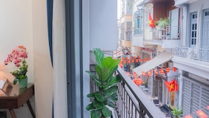 A balcony with a potted plant, a desk with a laptop, and a view of a street with buildings and red flags. - IL DIVO Hotel & Spa Hanoi Old Quarter (Hanoi)