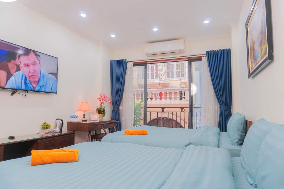 Habitació d'hotel amb televisió, escriptori amb làmpada, llit amb roba de llit blava i balcó amb cortines blaves.