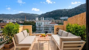 A balcony with a table, two sofas, and a view of buildings and hills. - A Cozy Stay with Terrace in the Heart of Sorrento (Sorrento)