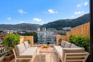 A balcony with a table, two sofas, and a view of buildings and hills. - A Cozy Stay with Terrace in the Heart of Sorrento (Sorrento)